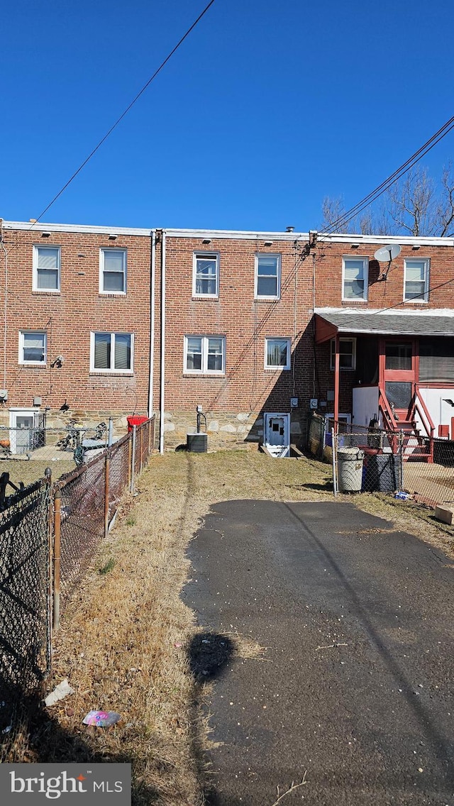 back of house featuring brick siding, central AC unit, and fence