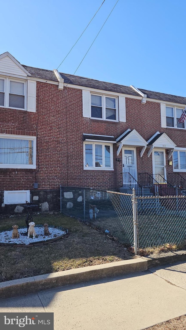 townhome / multi-family property featuring a fenced front yard and brick siding