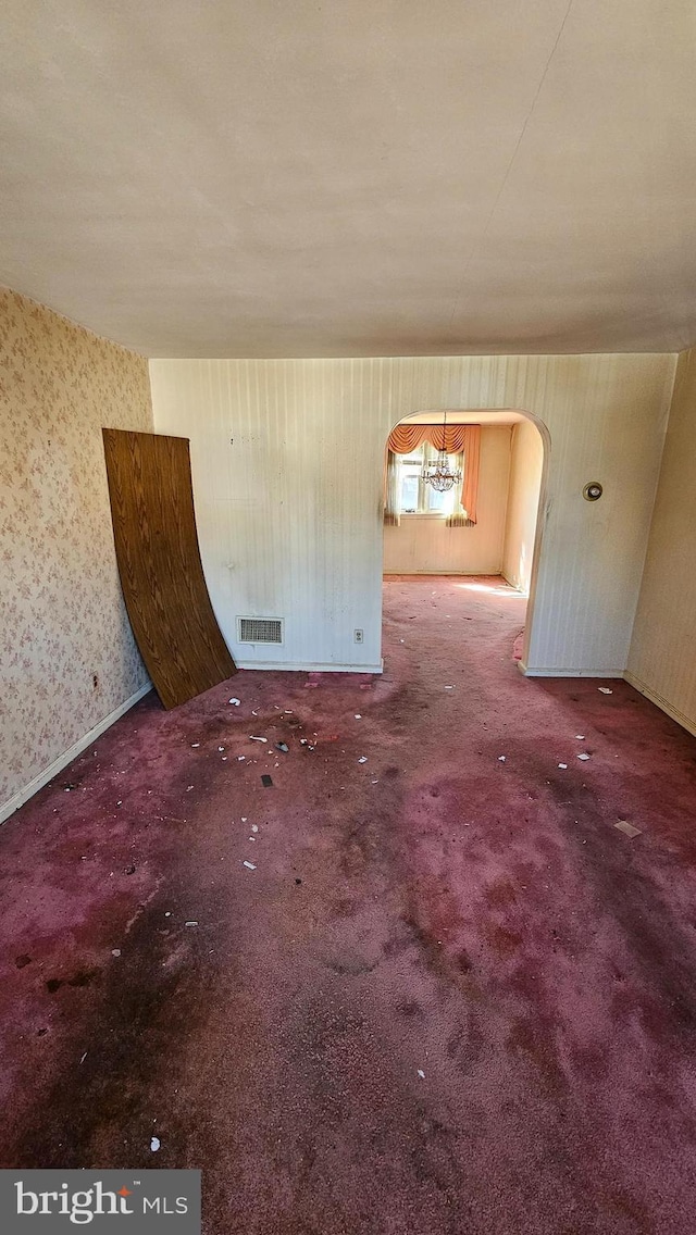 carpeted spare room with visible vents, arched walkways, and wallpapered walls