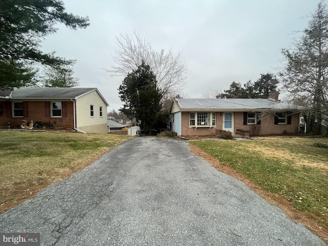 ranch-style house with aphalt driveway, a front lawn, brick siding, and a chimney