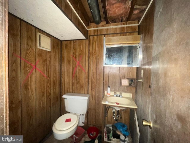 bathroom featuring wooden walls, toilet, and a sink