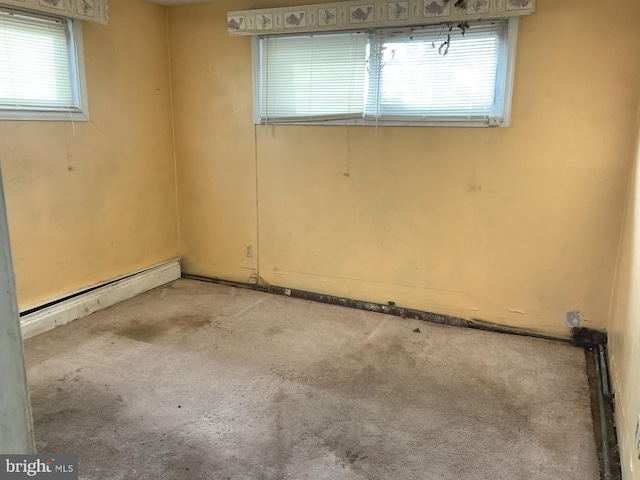 empty room featuring carpet floors, baseboard heating, and a healthy amount of sunlight