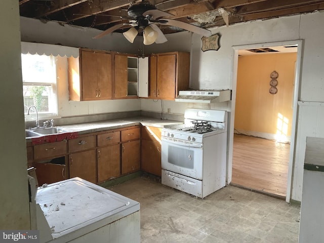 kitchen featuring brown cabinets, a ceiling fan, under cabinet range hood, a sink, and white range with gas stovetop