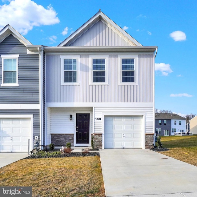 view of front of property featuring board and batten siding, a front yard, a garage, stone siding, and driveway