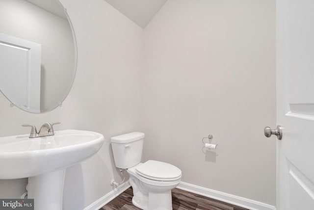 half bath with toilet, wood finished floors, baseboards, and a sink