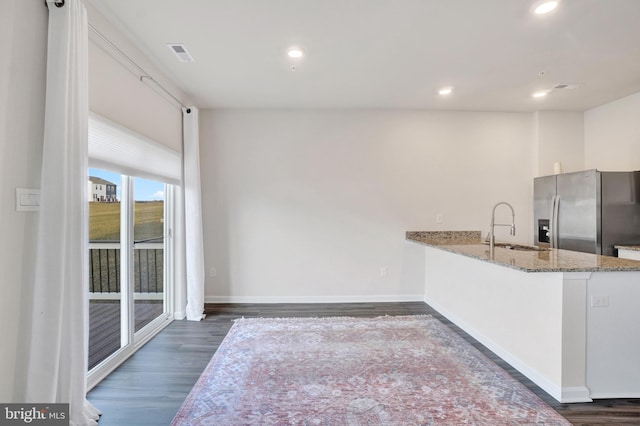 kitchen featuring light stone countertops, visible vents, dark wood-style flooring, a sink, and stainless steel refrigerator with ice dispenser