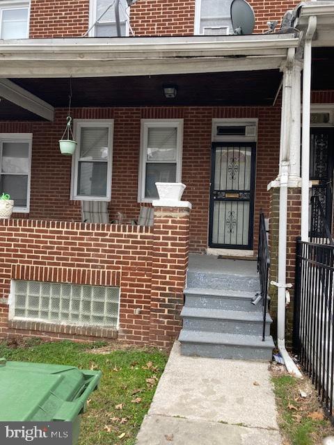 doorway to property featuring brick siding, a porch, and fence