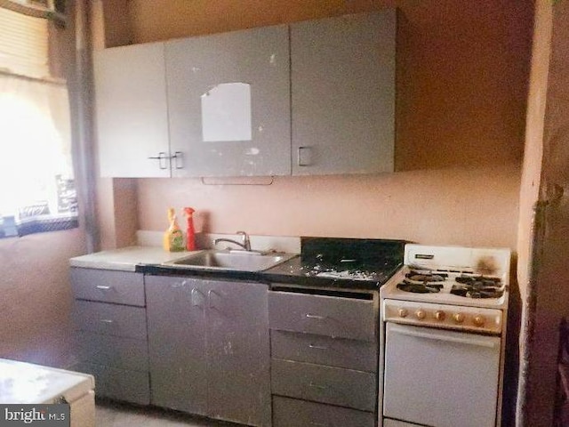 kitchen with gray cabinetry, gas range gas stove, and a sink