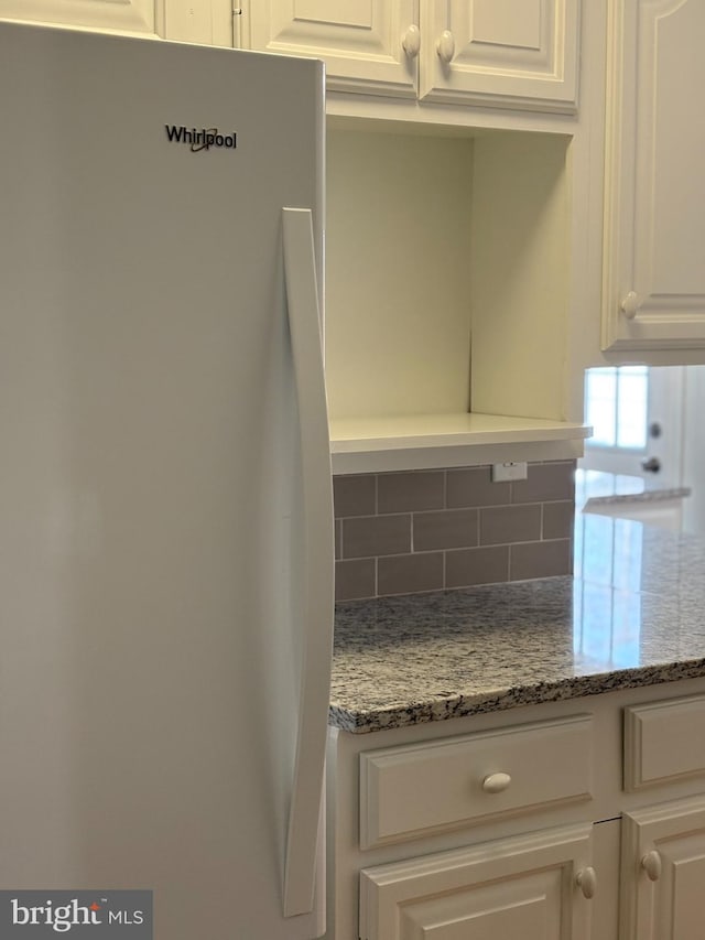 details featuring light stone counters, tasteful backsplash, white cabinets, and freestanding refrigerator