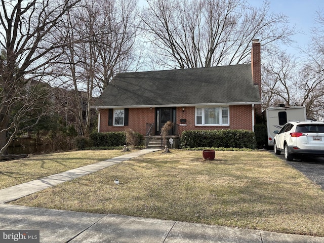 view of front facade with brick siding, a chimney, a front yard, and a shingled roof