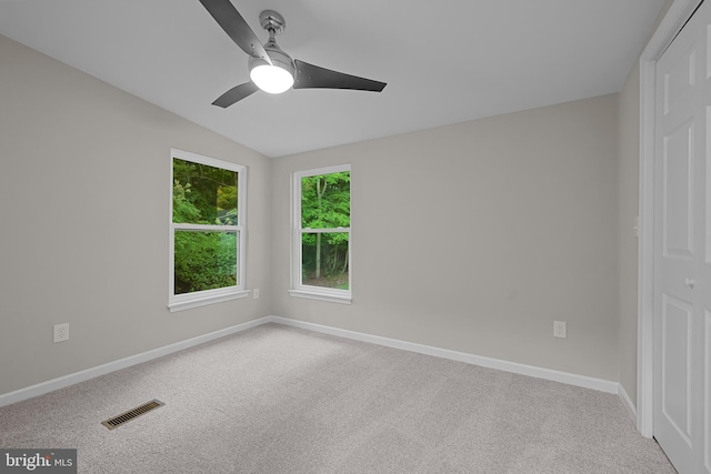 carpeted empty room with vaulted ceiling, baseboards, visible vents, and ceiling fan