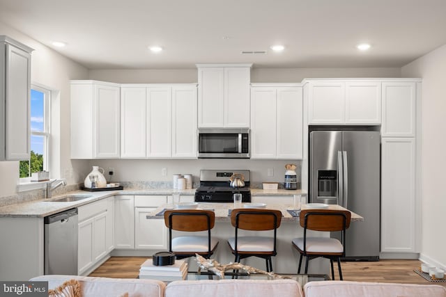 kitchen with visible vents, a kitchen breakfast bar, white cabinets, stainless steel appliances, and a sink