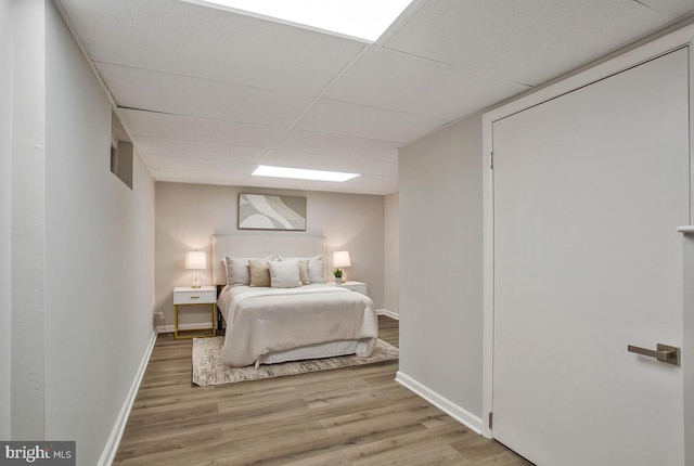 bedroom with a paneled ceiling, baseboards, and wood finished floors