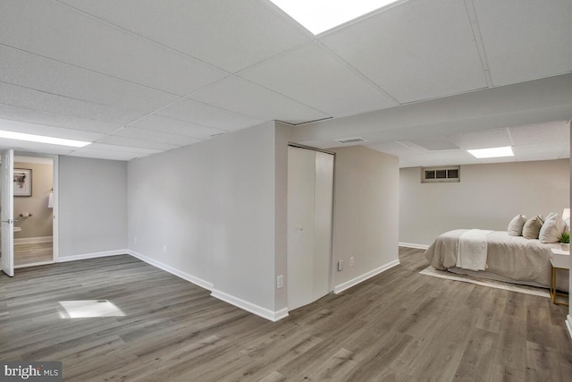 unfurnished bedroom with baseboards, a paneled ceiling, visible vents, and wood finished floors