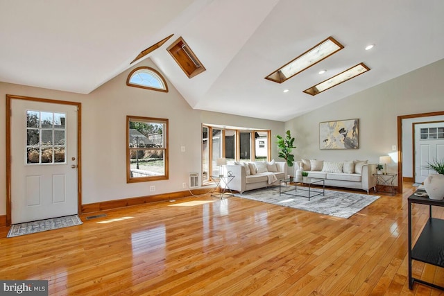 living room featuring baseboards, visible vents, light wood finished floors, high vaulted ceiling, and a skylight