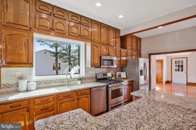 kitchen with brown cabinetry, light stone countertops, stainless steel appliances, and a sink