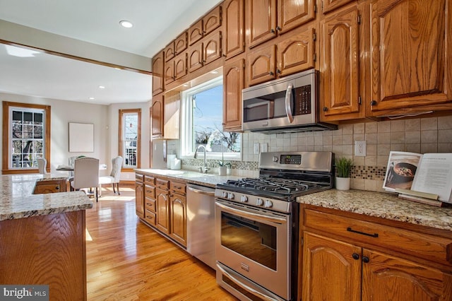 kitchen featuring light wood-style flooring, brown cabinetry, light stone countertops, and stainless steel appliances