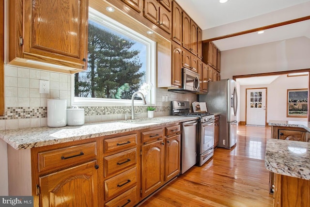 kitchen with brown cabinets, a sink, light stone counters, appliances with stainless steel finishes, and light wood finished floors