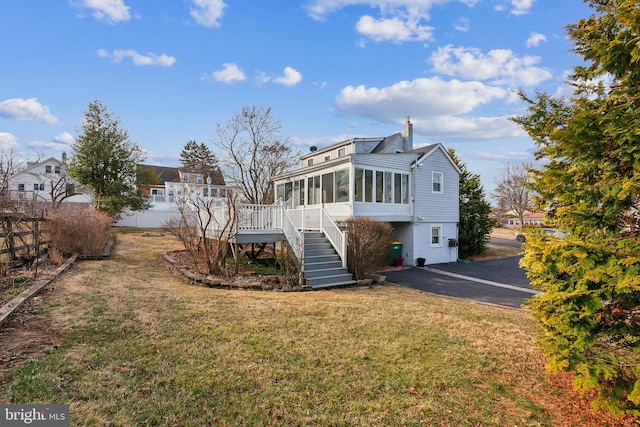 rear view of house featuring fence, driveway, a sunroom, stairs, and a lawn