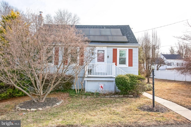 view of front of house featuring fence, solar panels, a front yard, and a shingled roof