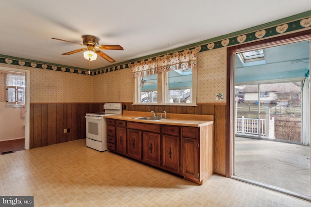 kitchen with white electric range oven, a skylight, a sink, brick patterned floor, and wainscoting