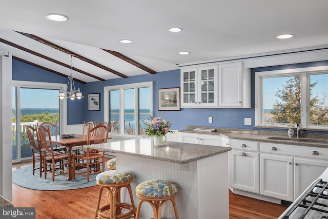 kitchen featuring wood finished floors, white cabinetry, lofted ceiling with beams, and a sink