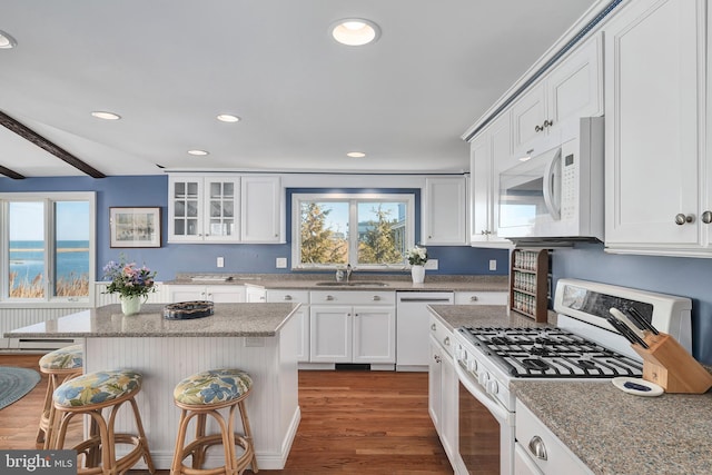 kitchen with white appliances, radiator, wood finished floors, white cabinets, and a kitchen bar