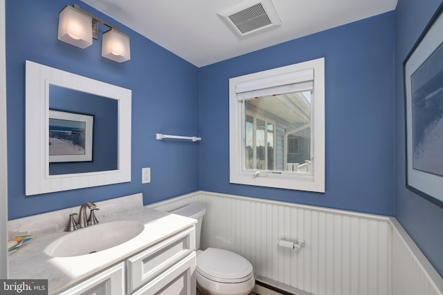 bathroom featuring visible vents, toilet, vanity, and a wainscoted wall