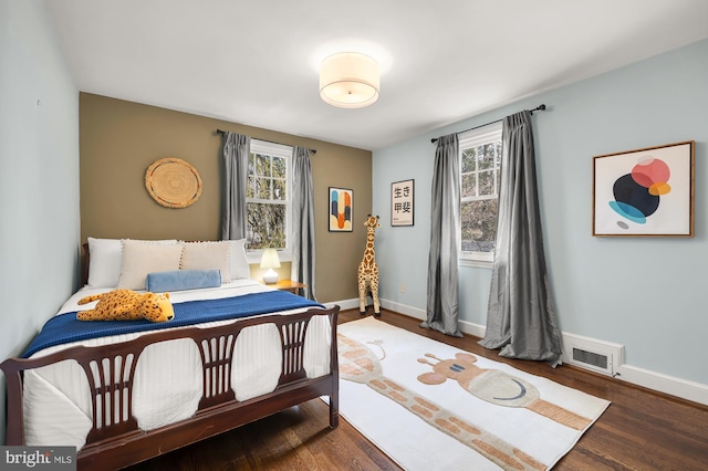 bedroom featuring visible vents, multiple windows, baseboards, and wood finished floors