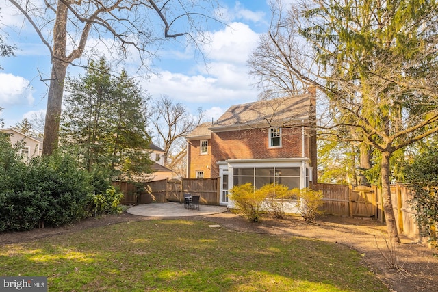 rear view of house featuring brick siding, a lawn, a fenced backyard, a sunroom, and a patio area