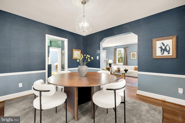 dining room featuring a notable chandelier, wood finished floors, arched walkways, baseboards, and an accent wall