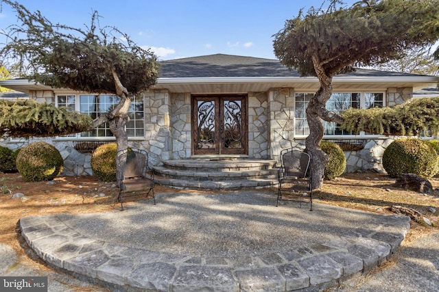 doorway to property with stone siding and roof with shingles