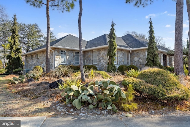 view of property exterior featuring stone siding and roof with shingles