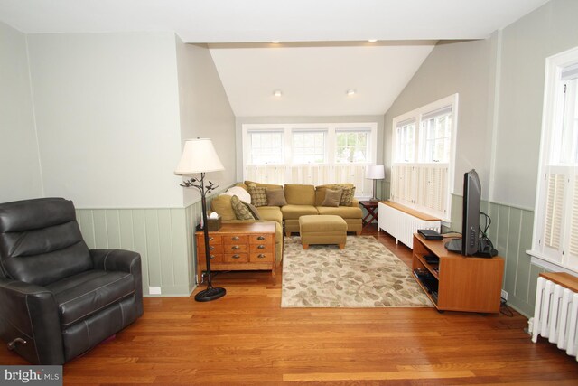 living area featuring a wainscoted wall, radiator, lofted ceiling, and wood finished floors