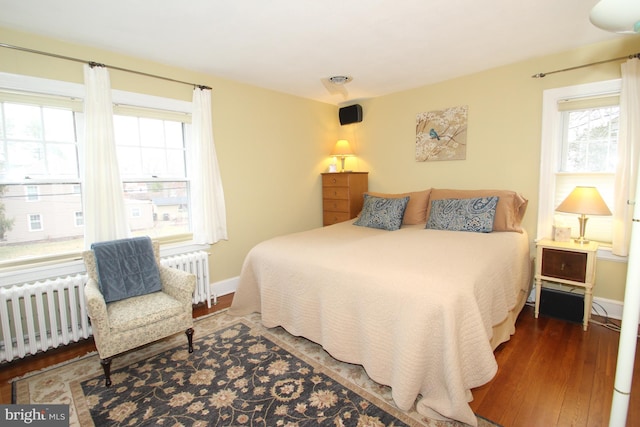 bedroom with multiple windows, radiator heating unit, and wood finished floors