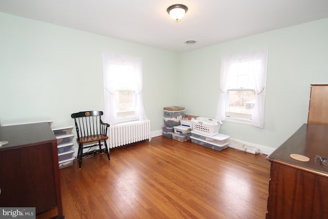 sitting room featuring baseboards, radiator, a healthy amount of sunlight, and wood finished floors