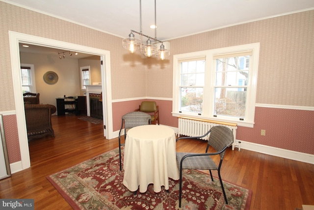 living area with wallpapered walls, radiator heating unit, ornamental molding, a fireplace, and wood finished floors