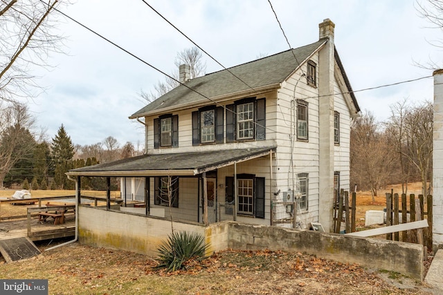 view of front facade with a porch, a chimney, and roof with shingles