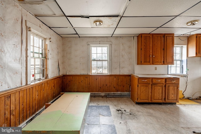 kitchen featuring a drop ceiling, a wainscoted wall, and brown cabinets