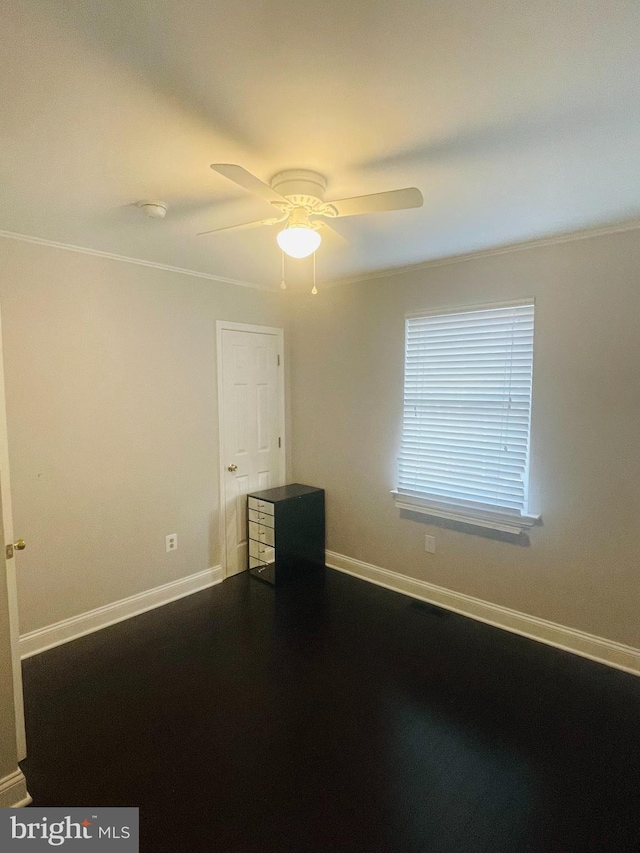 spare room featuring baseboards, ceiling fan, dark wood finished floors, and crown molding