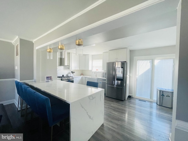 kitchen featuring light stone counters, appliances with stainless steel finishes, a peninsula, dark wood-style floors, and white cabinetry