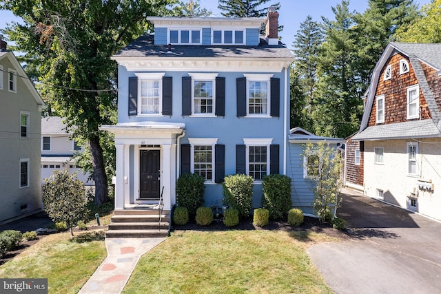 view of front of home featuring driveway, a chimney, a front yard, and a shingled roof