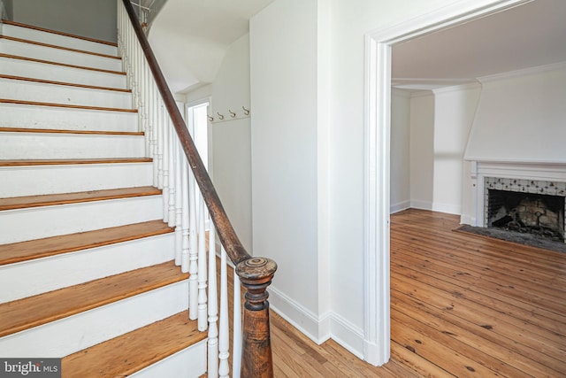 staircase featuring a fireplace, crown molding, baseboards, and hardwood / wood-style flooring