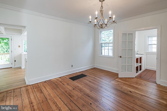 spare room featuring an inviting chandelier, visible vents, wood-type flooring, and ornamental molding