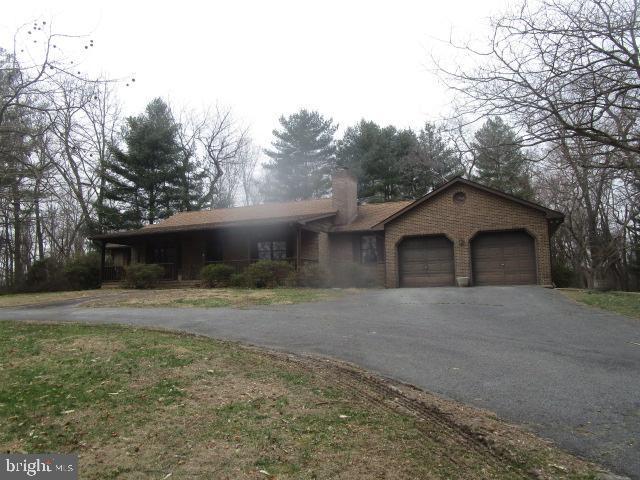 ranch-style house featuring aphalt driveway, brick siding, a garage, and a chimney