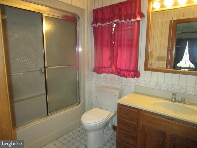 full bathroom with bath / shower combo with glass door, toilet, and vanity