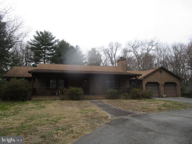 single story home with a chimney, an attached garage, a porch, and driveway