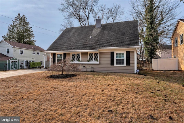 rear view of house with a lawn, roof with shingles, a chimney, and fence