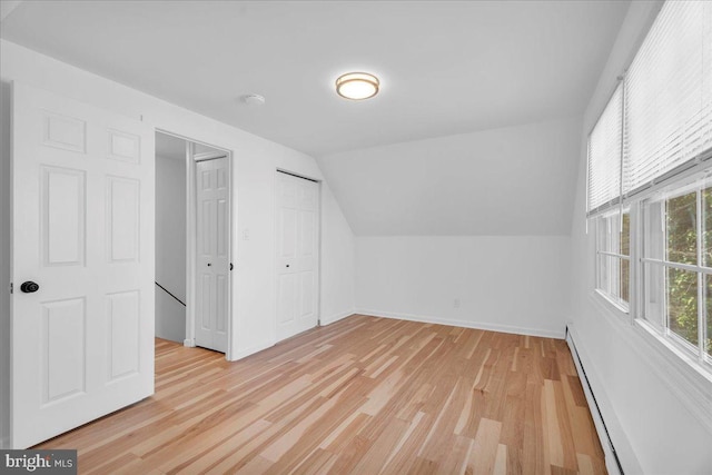 additional living space with a baseboard heating unit, vaulted ceiling, baseboards, and light wood-type flooring