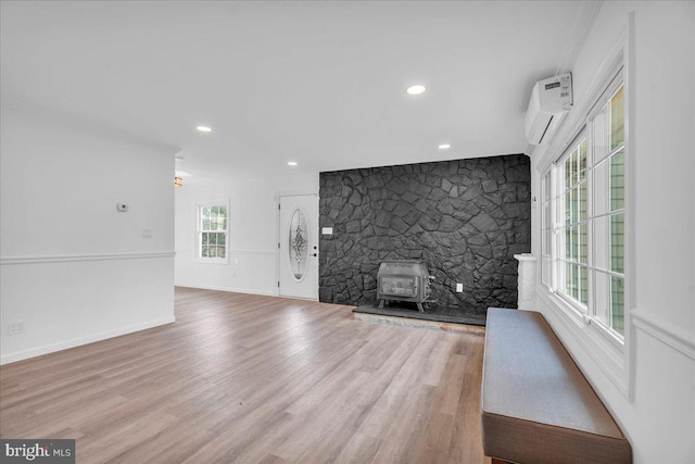 interior space with a wall unit AC, wood finished floors, baseboards, a wood stove, and recessed lighting